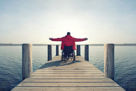 Bilde av mann i rullestol med åpne armer som ser utover horisonten.