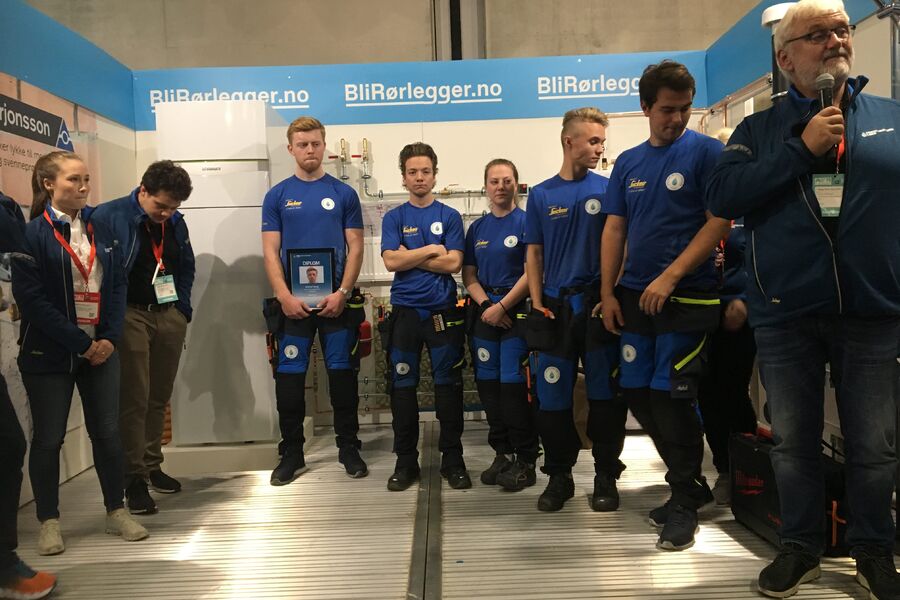 Alle deltagerne samlet på podiet under utdelingen av beviset på bestått svenneprøve, og kåringen av Norgesmester 2019 i rørleggerfaget. Vinneren Erlend Haug fra Lillestrøm Rørleggerbedrift AS er nummer tre fra venstre.  Utdelingen ble ledet av hoveddommer Helge Andersen ( til høyre)