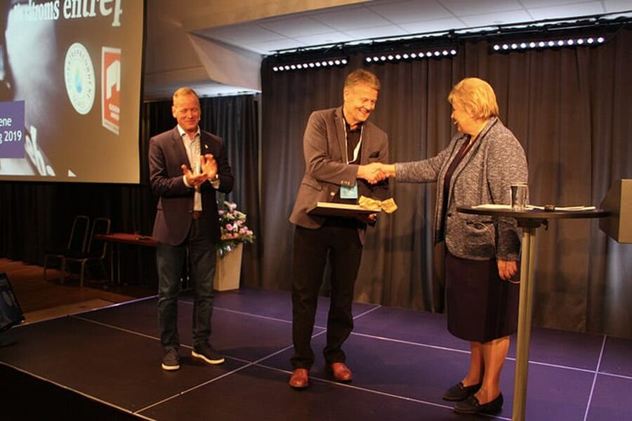 Tor Backe mottar diplom og medalje av statsminister Erna Solberg, mens styreleder Torkild Korsnes i Rørentreprenørene Norge applauderer.