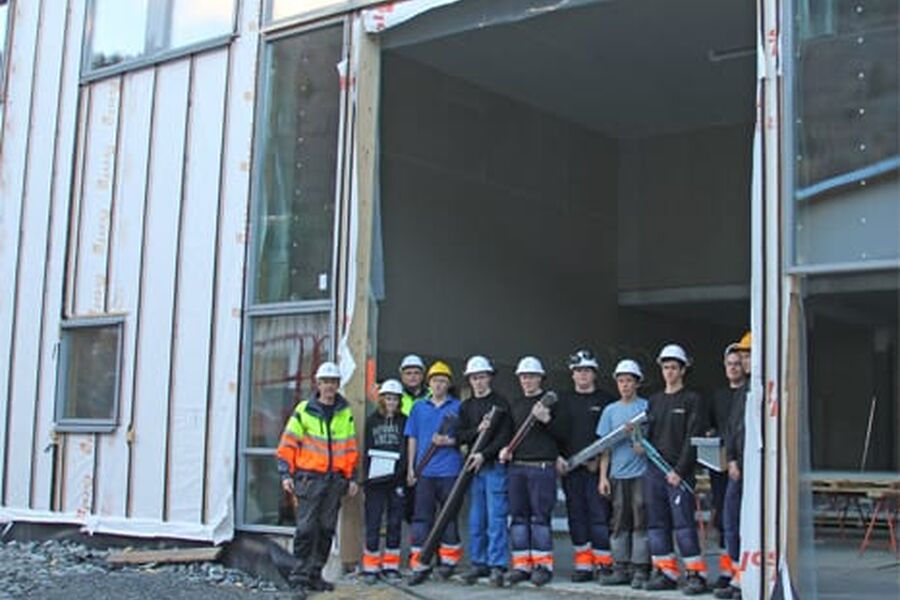 Elever og lærer Oddbjørn Skjerdal ved Sogndal videregående skole foran en av de nye hallene som nå bygges på skolen.