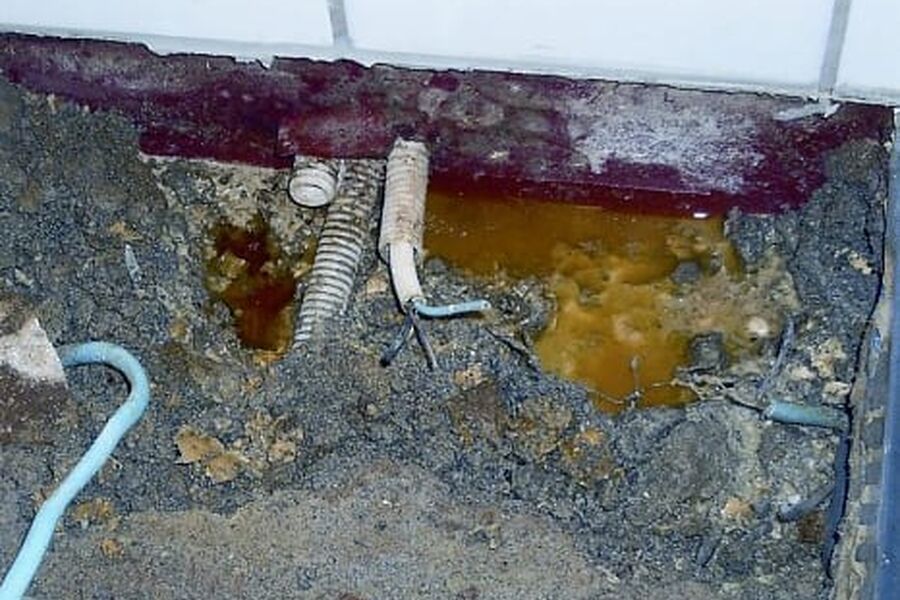Lekkasjepunkter i golvmembran ved gjennomføring av rør og elkabler Det er underliggende membran som er ført opp på veggen, men den er punktert på grunn av gjennomføringene. Det står vann i og under påstøpen. Vannet renner ut ved gjennomføringene. Foto: SINTEF Byggforsk