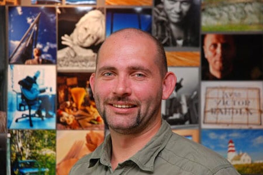 Thor-Jostein Egeland med med bildeveggen hos Skarland Press i bakgrunnen.