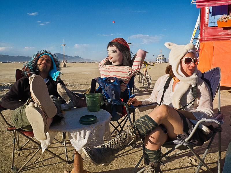 Tre mennesker sitter og slapper av. Men vent litt, er de ikke litt rart kledd? Og én av dem er jo en dukke! Det er mange historier å fortelle på Burning Man-festivalen. (Foto: Otto von Münchow)