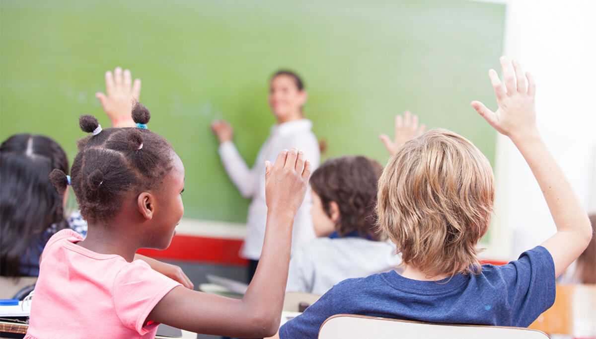 Portrait of children raised their hands in a multi ethnic classroom.