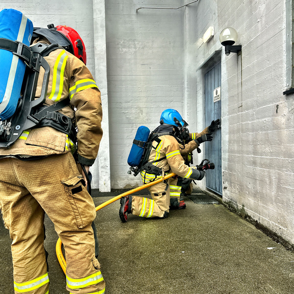 brannøvelse med tre brannmenn som går inn ei røykfylt dør