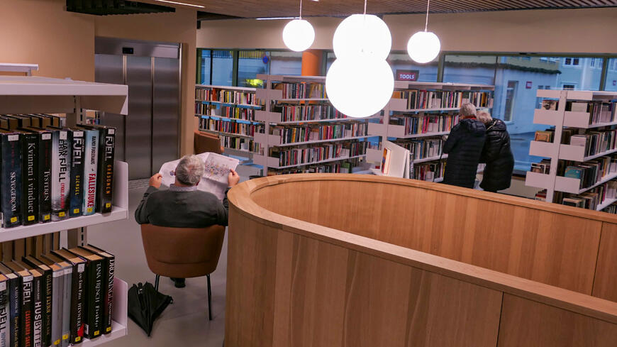 Biblioteket på innsiden med besøkenende som leser avis og ser etter bøker