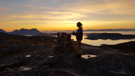 Dame på fjelltopp i solnedgang