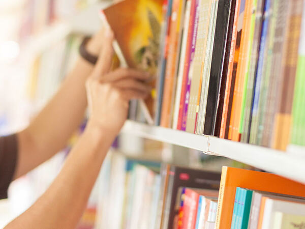 En hånd som henter en bok ut av en bokhylle
